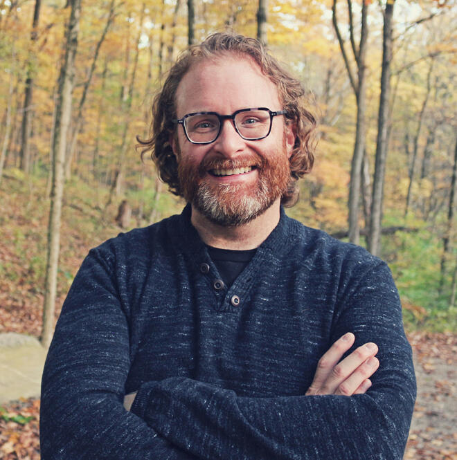 Josh Smith, professional voice actor, wearing a dark black sweater suit with a friendly expression.